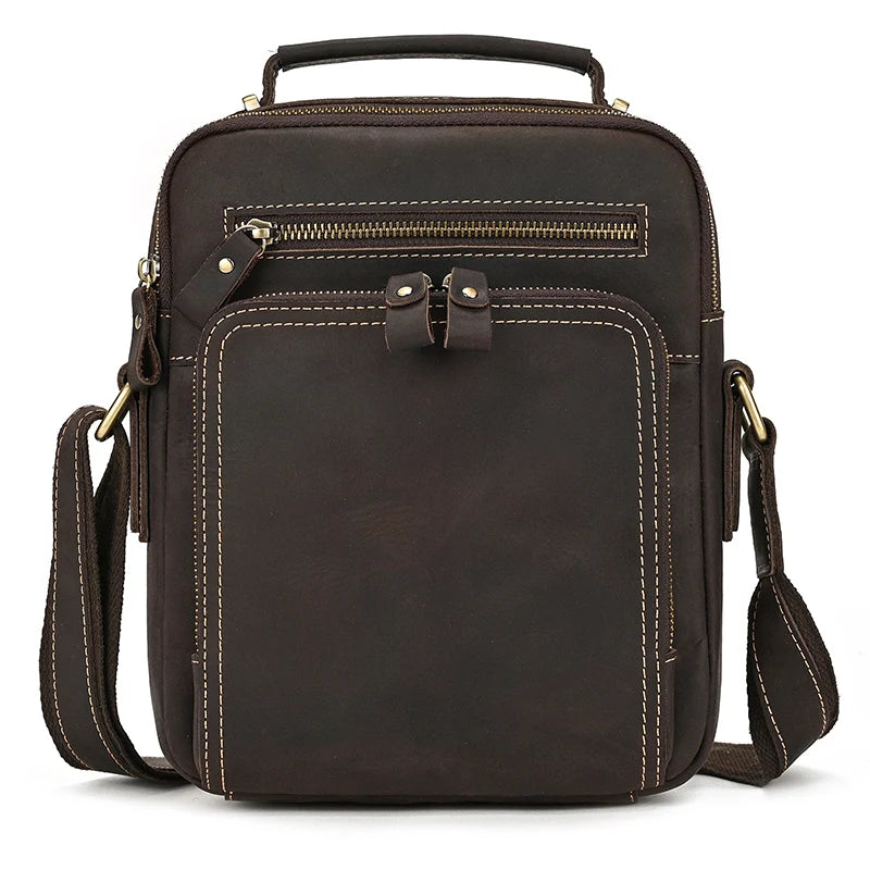 The Dark Brown Leather Shoulder Bag features a sturdy top handle, an adjustable shoulder strap, one front zipper pocket, and prominent stitching. Crafted from genuine cowhide leather, the front also boasts a larger pocket with two buckle details and durable alloy hardware.