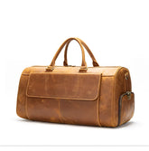 The Vintage Genuine Leather Travel Duffle Bag is a tan leather duffle crafted from genuine cow leather, featuring two short handles. It boasts a large front flap pocket and a side zipper pocket, embodying a classic design. Its smooth texture and spacious interior lend this premium travel bag an elegant yet functional appeal.