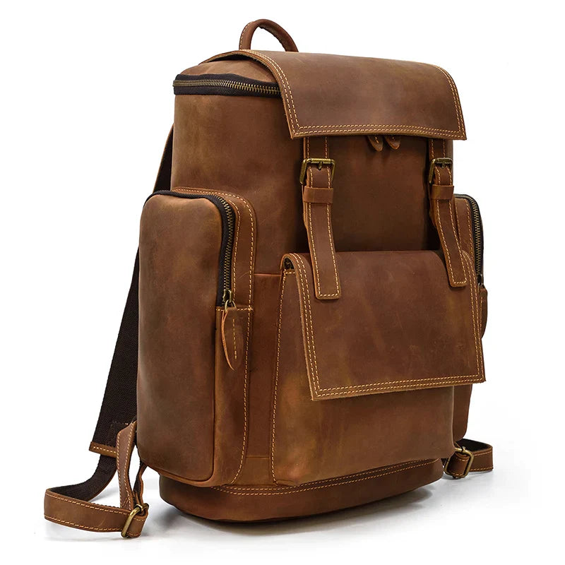 The Vintage Leather Travel Backpack is made from genuine cowhide leather and features large front and side pockets, gold hardware, adjustable black shoulder straps, a flap closure with buckles, and a laptop compartment. It's elegantly displayed against a plain white background.