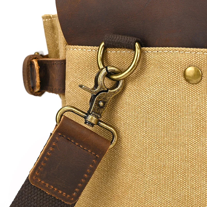 Close-up of a brown leather strap on the Canvas & Leather Vintage Messenger Bag features detailed stitching, attached to a beige canvas with a brass hook and ring, secured by a leather flap and brass button.