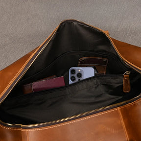 The Weekender Duffle 22 Leather Travel Bag in open brown genuine cowhide leather reveals its contents: a smartphone in a protective case, a closed brown pocket wallet, and a passport stored in separate inner compartments. The bag boasts a black fabric interior with zippers and pockets for optimal organization.