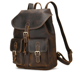 The Genuine Leather Vintage Backpack, in brown softback leather, features two front pockets with buckle closures. It has a flap closure secured by a buckle and adjustable shoulder straps, offering a casual, vintage charm with its rugged genuine leather appearance.