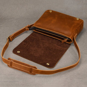 The Vintage Leather Shoulder Bag is on display, featuring a comfortable shoulder strap and a rich brown hue. The front flap is open, revealing an inner pocket secured by a zipper. The interior is lined with darker brown material, and metal snaps are visible on the flap and corners of the bag, exuding timeless style.