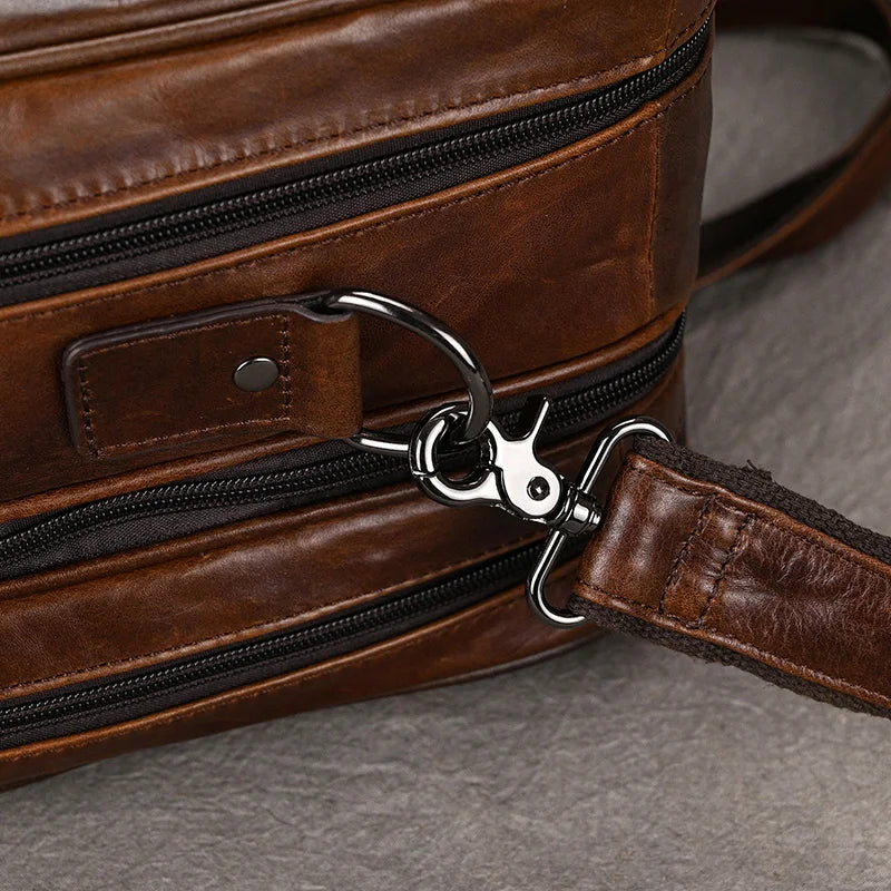 Close-up of the Leather 17" Business Travel Briefcase showcasing a metal clasp and ring attachment. The bag features visible stitching and a zippered pocket, making it ideal for business travel. The glossy leather finish enhances its sleek look, while the clasp is connected to a strap. Background surface is gray.