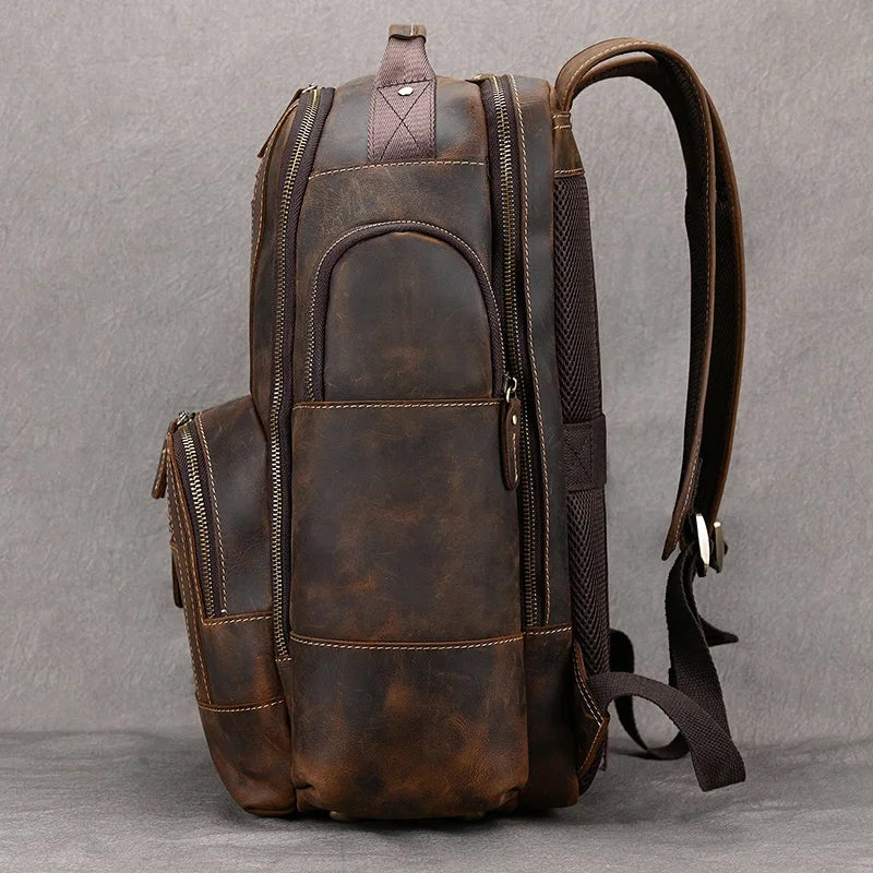 A side view of the Vintage Leather Travel Backpack, showcasing its large, brown vintage leather design with padded shoulder straps and multiple zippered compartments against a gray background. The detailed stitching and slightly distressed texture make it perfect for carrying your travel essentials.