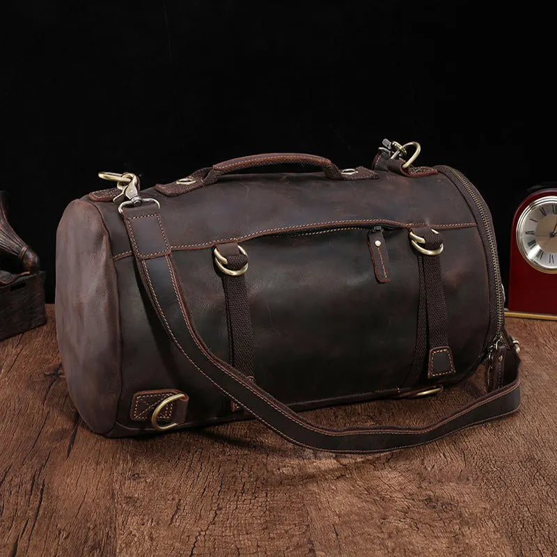 A Vintage Leather Travel Backpack crafted from genuine cowhide leather with metal buckles and a shoulder strap rests on a wooden surface. Perfect for the stylish traveler, a small clock is partially visible in the background.