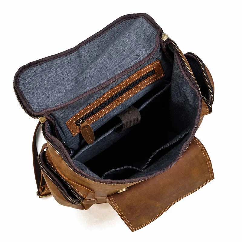 The Vintage Leather Travel Backpack, made from genuine brown cowhide leather with a blue fabric lining, offers ample storage with multiple compartments, including a large main section for laptops, a smaller zippered pocket, and pen holder. The open design highlights its spacious capacity.