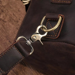 Close-up of a Vintage Leather Travel Backpack in dark brown genuine cowhide leather showcases a metal clasp and detailed stitching on the leather strap. This versatile backpack, ideal for the stylish traveler, features a clasp attached to a metal ring, resting elegantly on a wooden surface.