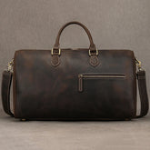 The Leather Travel Duffle is a large, dark brown bag made from genuine leather, featuring dual top handles, an adjustable shoulder strap, a front zipper pocket, and metal hardware accents. The vintage-inspired design stands out against a gray background.