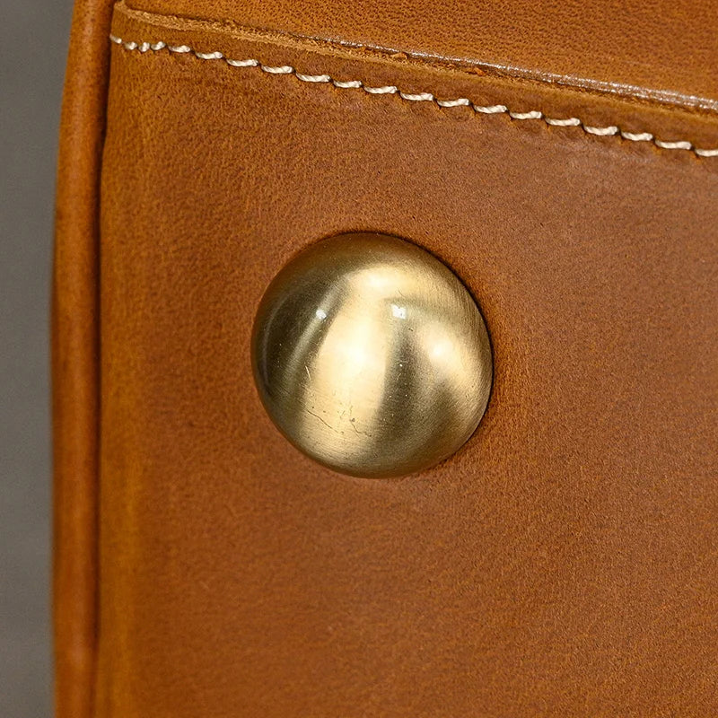 A close-up of a brass-riveted button on the Leather Travel Duffle highlights its genuine leather craftsmanship, featuring a smooth texture with visible edge stitching.