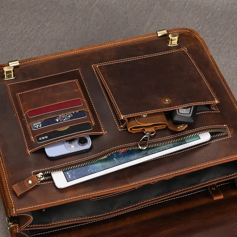 The Vintage Leather Briefcase displays its compartments, revealing credit cards, a smartphone, a car key, and a tablet neatly organized inside. The bag boasts multiple pockets, a dedicated laptop compartment, a zipper section, and secure brass clasps. All of this is set against a grey surface that enhances the professional appearance of the briefcase.