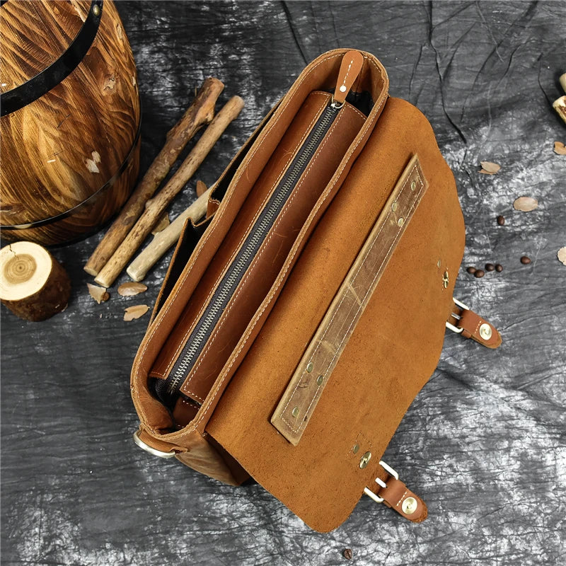 A top-down view of an open Leather 14" Briefcase Shoulder Bag crafted from brown genuine cowhide, featuring a zipper compartment in the center. The bag is placed on a dark, textured surface near a wooden barrel and several cut wooden logs and sticks.