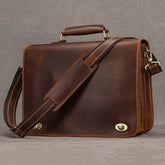 Introducing the Vintage Leather Briefcase, crafted from genuine leather and featuring a dedicated laptop compartment with a sturdy handle. This professional accessory is enhanced by an adjustable shoulder strap and adorned with gold-tone hardware, including two front clasps and a side zipper, all set against a sophisticated grey backdrop for an elegant look.