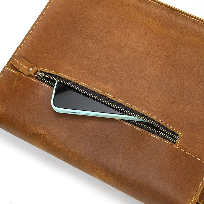 A close-up of the **Vintage Shoulder Bag** shows a zippered pocket partially open, revealing the edge of a smartphone inside. The genuine cowhide leather bag features visible stitching along the seams, and the metallic zipper glistens. The bag is placed on a white surface.