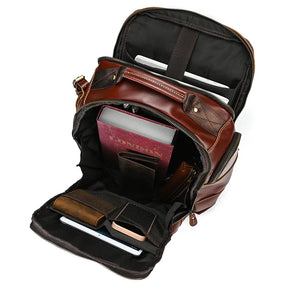 A Vintage Leather Travel Backpack with an open view showcasing its well-organized interior compartments. Visible items inside include a red book, a tablet, a smartphone, a charger, and a wallet. This backpack is crafted from genuine cowhide leather and features multiple pockets and sections, highlighting its ample storage space for personal belongings.