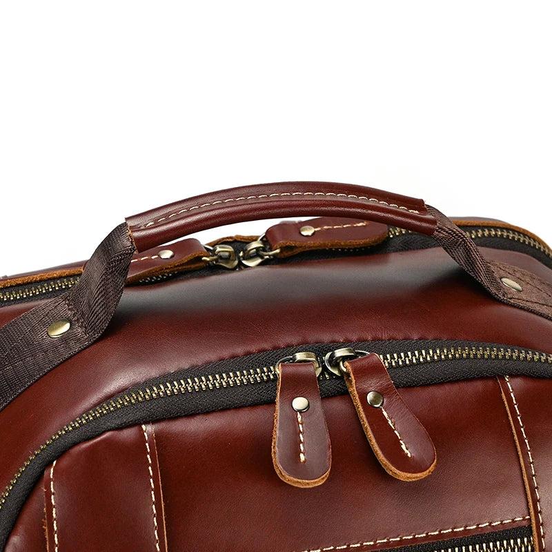 Close-up image of the Vintage Leather Travel Backpack showcasing the handle and top zipper compartment with metallic zippers. The genuine cowhide leather bag features beige stitching accents and sturdy black fabric straps attached to the handle, offering ample storage for all your essentials.