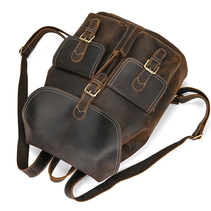 Introducing the Genuine Leather Vintage Backpack: a classic brown softback crafted from high-quality leather. It features two buckle-closure front pockets and a spacious bottom pocket. The backpack is designed with adjustable shoulder straps and detailed stitching, offering a rugged yet casual and stylish appearance.