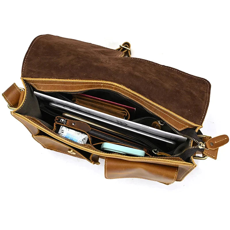 Top view of an open Leather Business Travel Shoulder Bag with multiple compartments. Inside, a silver laptop, a smartphone, a wallet, a pair of glasses, and several small items are visible. The bag, made from genuine cowhide leather and featuring alloy hardware, has a brown inner lining and appears spacious and organized.