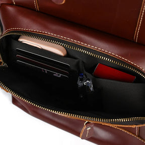 A close-up view of the partially opened Vintage Leather Travel Backpack reveals its ample storage. Inside the genuine cowhide leather bag, several compartments neatly hold various items, including a smartphone, cards, a red notebook, and pens. The brown backpack's zipper is partially opened.