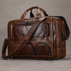 The Leather 17" Business Travel Briefcase is a brown genuine leather briefcase that is perfect for business travel. It boasts multiple zippered compartments and laptop pockets, providing ample storage space. Featuring a top handle and an adjustable shoulder strap, this bag offers versatile carrying options. Its polished finish lends it a classic and sophisticated appearance.