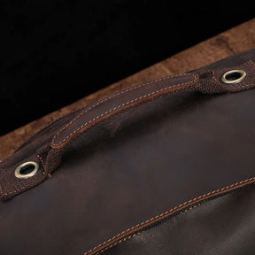 Close-up of a genuine cowhide leather handle on the Vintage Leather Travel Backpack, featuring visible stitching and metal eyelets against a dark surface. The rich brown leather showcases a smooth texture and detailed craftsmanship, ideal for the stylish traveler.