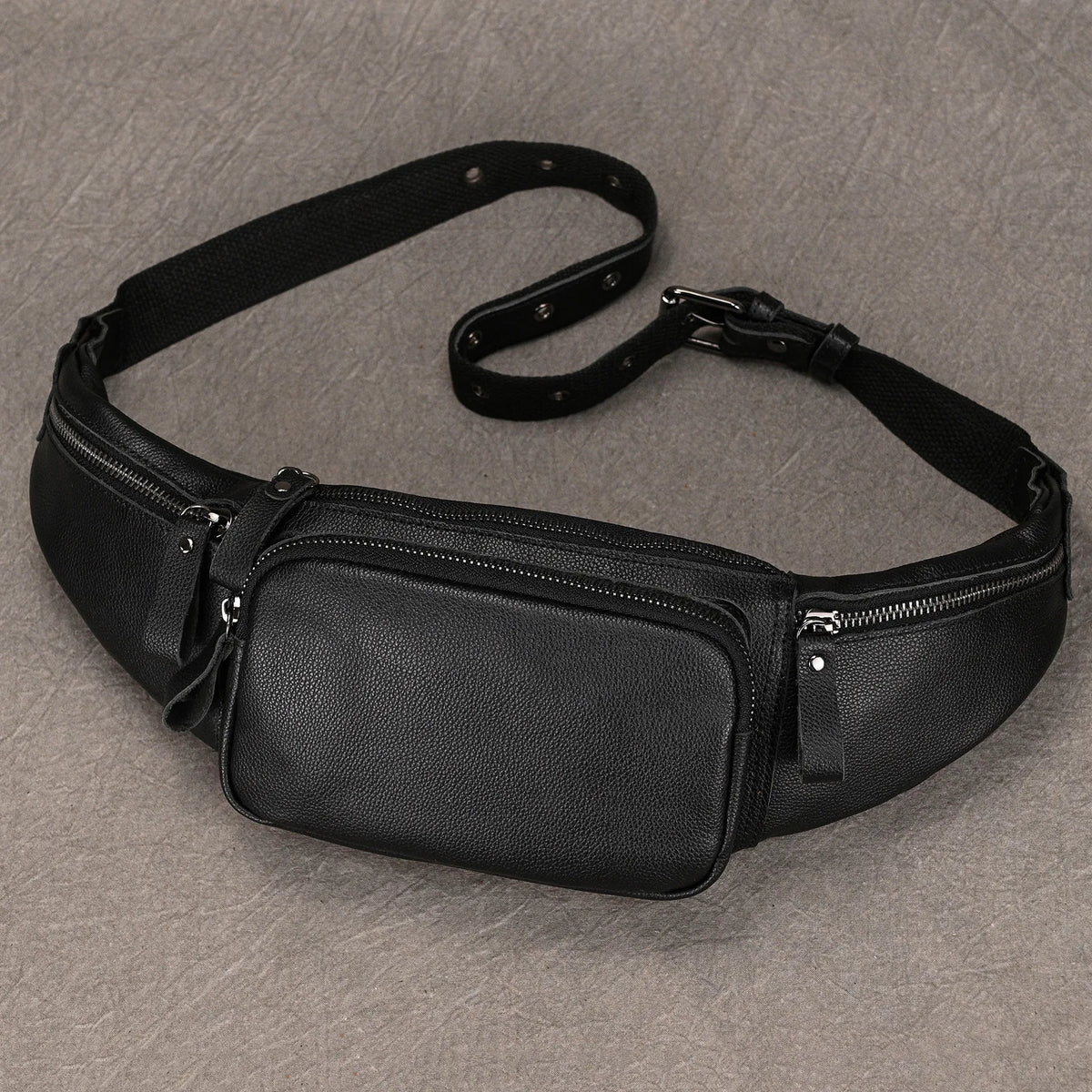 The Leather Belt Bag, crafted from genuine cowhide leather, is showcased against a textured gray backdrop. Featuring multiple zippered compartments and an adjustable strap, the central pocket stands out boldly with smaller side pockets on either side, making it ideal for the fashion expert on the go.