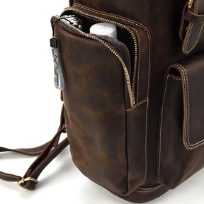 The Vintage Leather Travel Backpack features genuine cowhide leather, visible stitching, a side pocket with an unzipped water bottle, fabric zipper pulls, side straps, and a hidden laptop compartment for convenience.