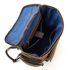 The Vintage Leather Travel Backpack, made from genuine cowhide leather, has a flap with a blue fabric interior. It features a laptop compartment and pockets for organization, along with sturdy zippers and adjustable straps, making it ideal for carrying books or tech gear.