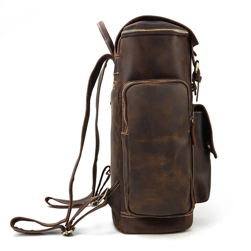 Side view of the Vintage Leather Travel Backpack made from genuine cowhide, showcasing a top handle, two straps, multiple pockets including a large front pocket with a flap, and a practical laptop compartment enhancing its rustic charm.