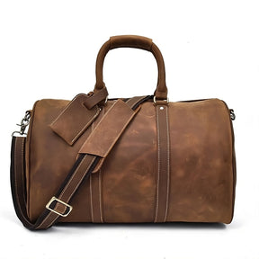 The Weekender 18 Leather Bag is a brown leather duffle with two sturdy handles and a detachable shoulder strap. Made from genuine cowhide leather, it showcases white stitching details and includes a matching luggage tag. With its spacious interior pockets, it is ideal for organized travel, all in a rustic finish.